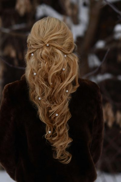 A woman with an intricate blonde hairstyle adorned with pearls, standing outdoors in winter.